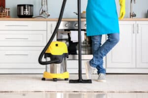 Young man with vacuum cleaner in kitchen