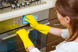 Cleaning the oven concept. Woman in gloves and an apron in the kitchen washing the oven door