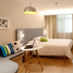 A bedroom inside an Airbnb rental with wooden floors, a bed with a white comforter, and a sitting area with a desk and a laptop.