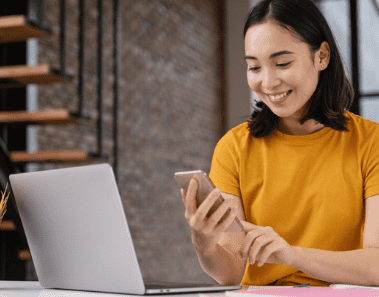 Woman holding a phone and looking at her laptop while scheduling professional Airbnb cleaning services.