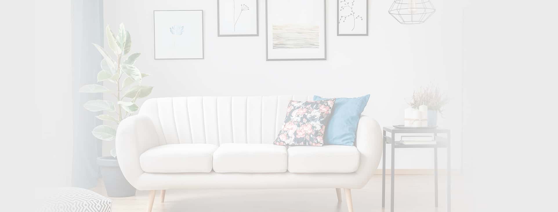 Living room of a rental home with a white couch that has a tall plant and a coffee table next to it.