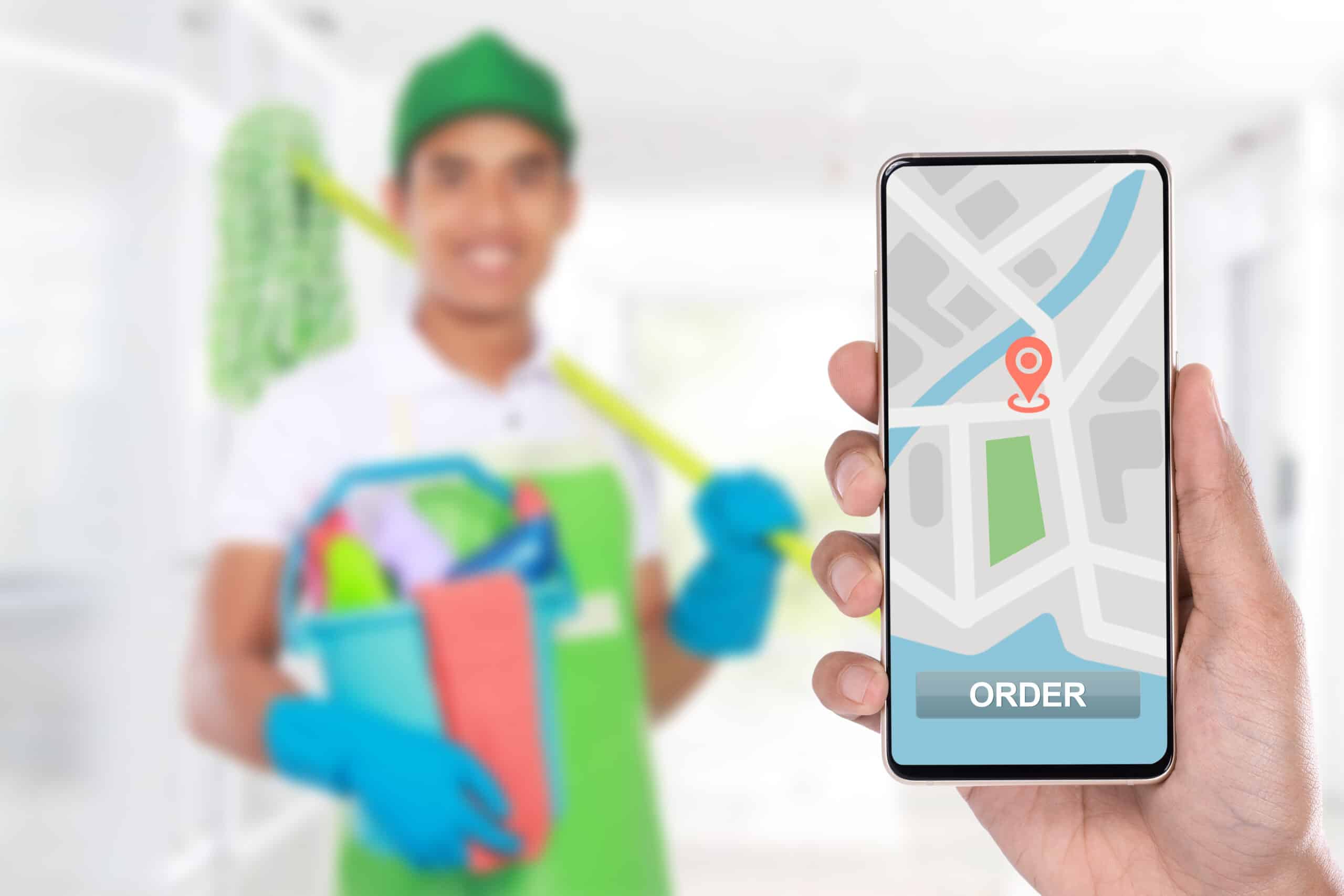 Person holding up a phone with a map. In the background there is a man with Airbnb cleaning products such as a mop and several cleaning agents.