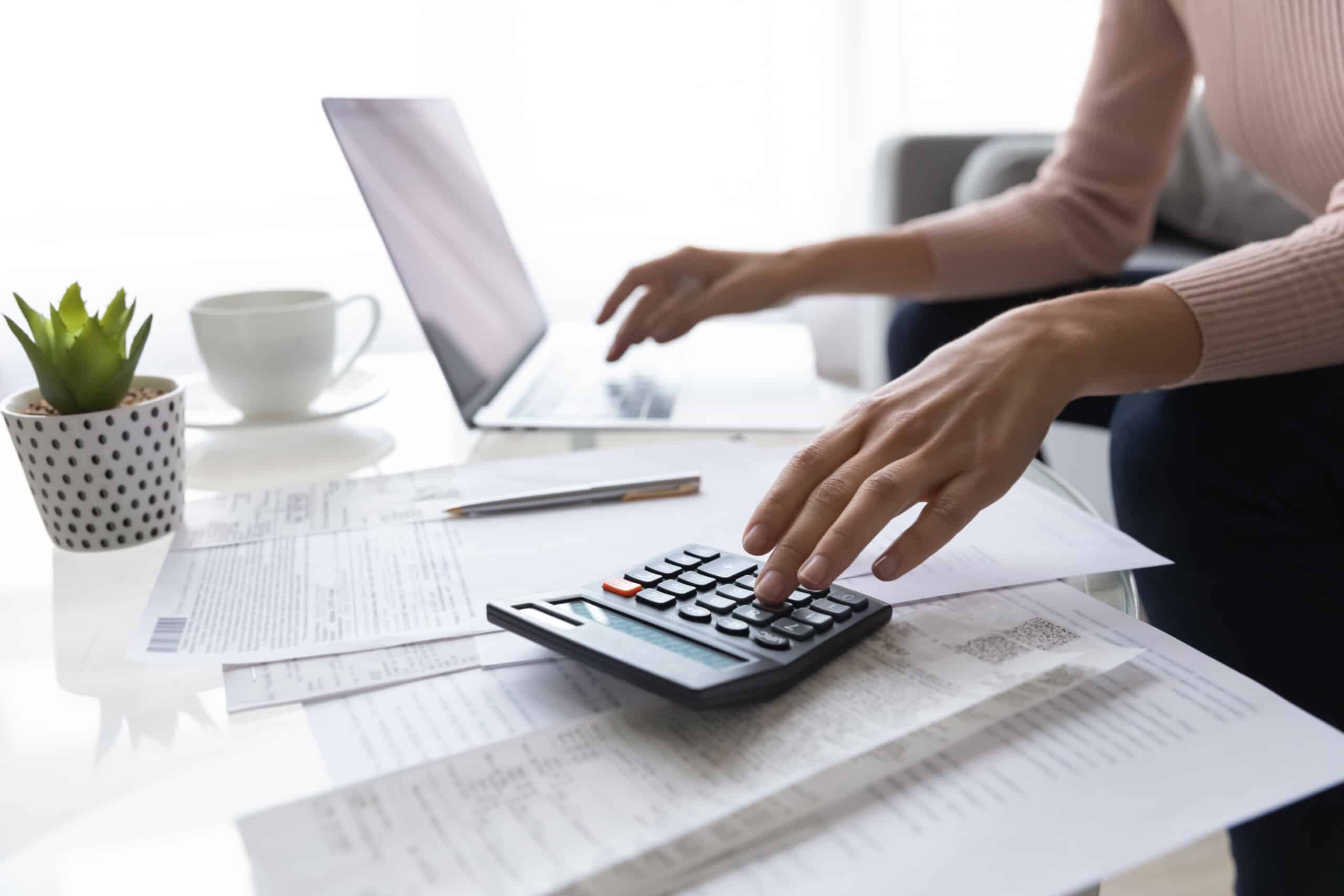 Woman calculating Airbnb cleaning service costs with a laptop and calculator.