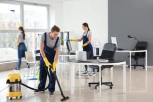 Three members of The Magic Helpers team dusting and vacuuming an office space.