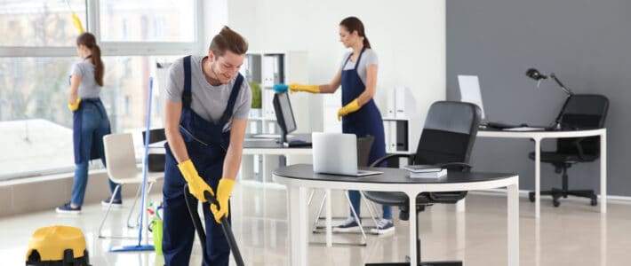 Three members of The Magic Helpers team dusting and vacuuming an office space.