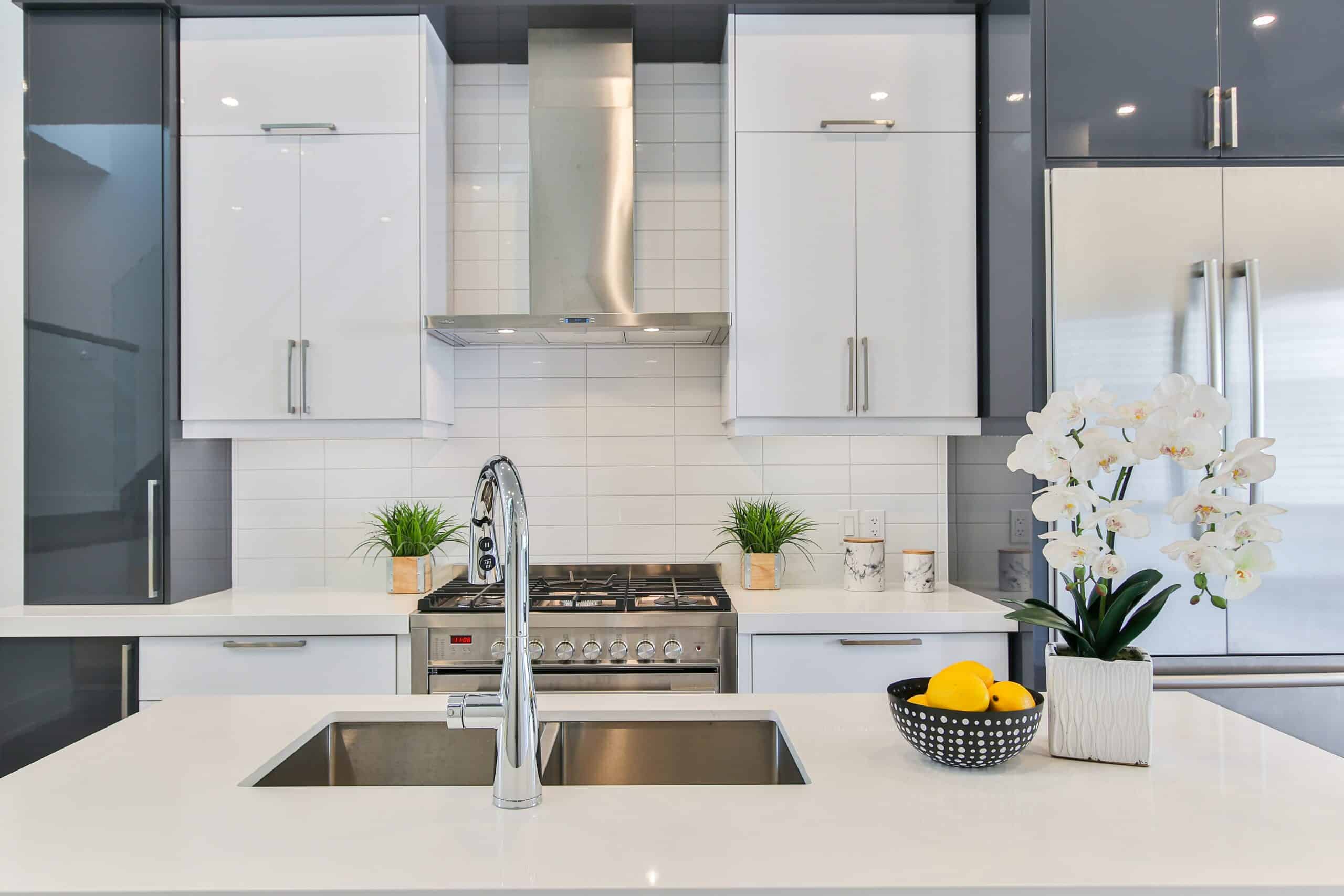 The Best Cleaning Materials for Different Surfaces Airbnb kitchen with white countertops, white backsplash, and a white orchid sitting next to a bowl of lemons.