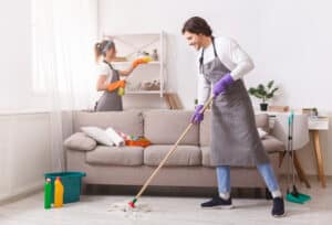 Two members of The Magic Helpers residential cleaning team mopping and dusting a customer's home.