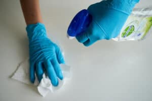 Person with gloves and a paper total wiping down a white counter with cleaning solution.