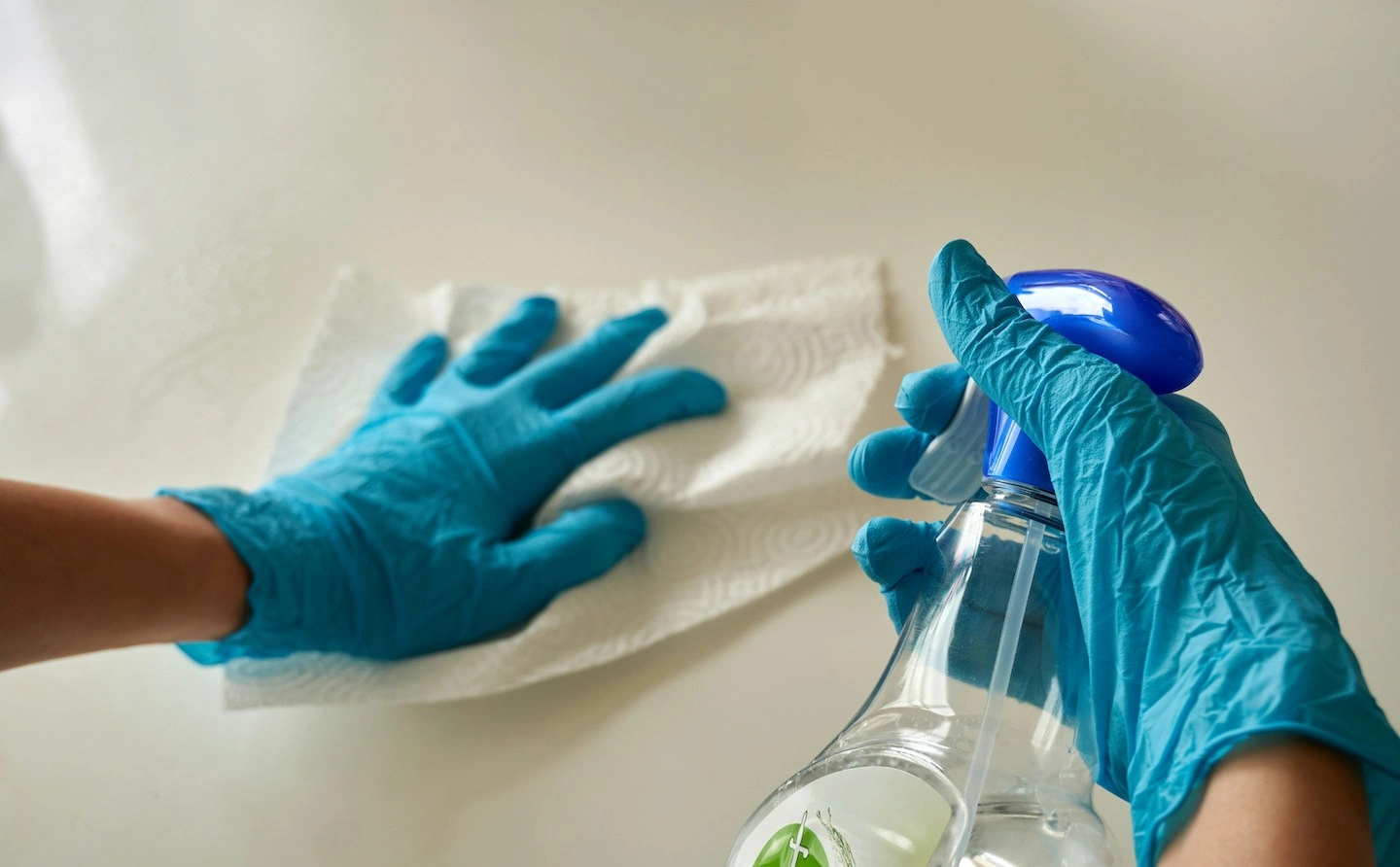 Person wearing blue gloves holding a clear spray bottle of cleaning product.
